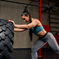 Fit Female Athlete Working Out With A Huge Tire, Turning And Fli